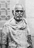 Small archival photograph of Sant Gadge Baba standing in patched clothes.