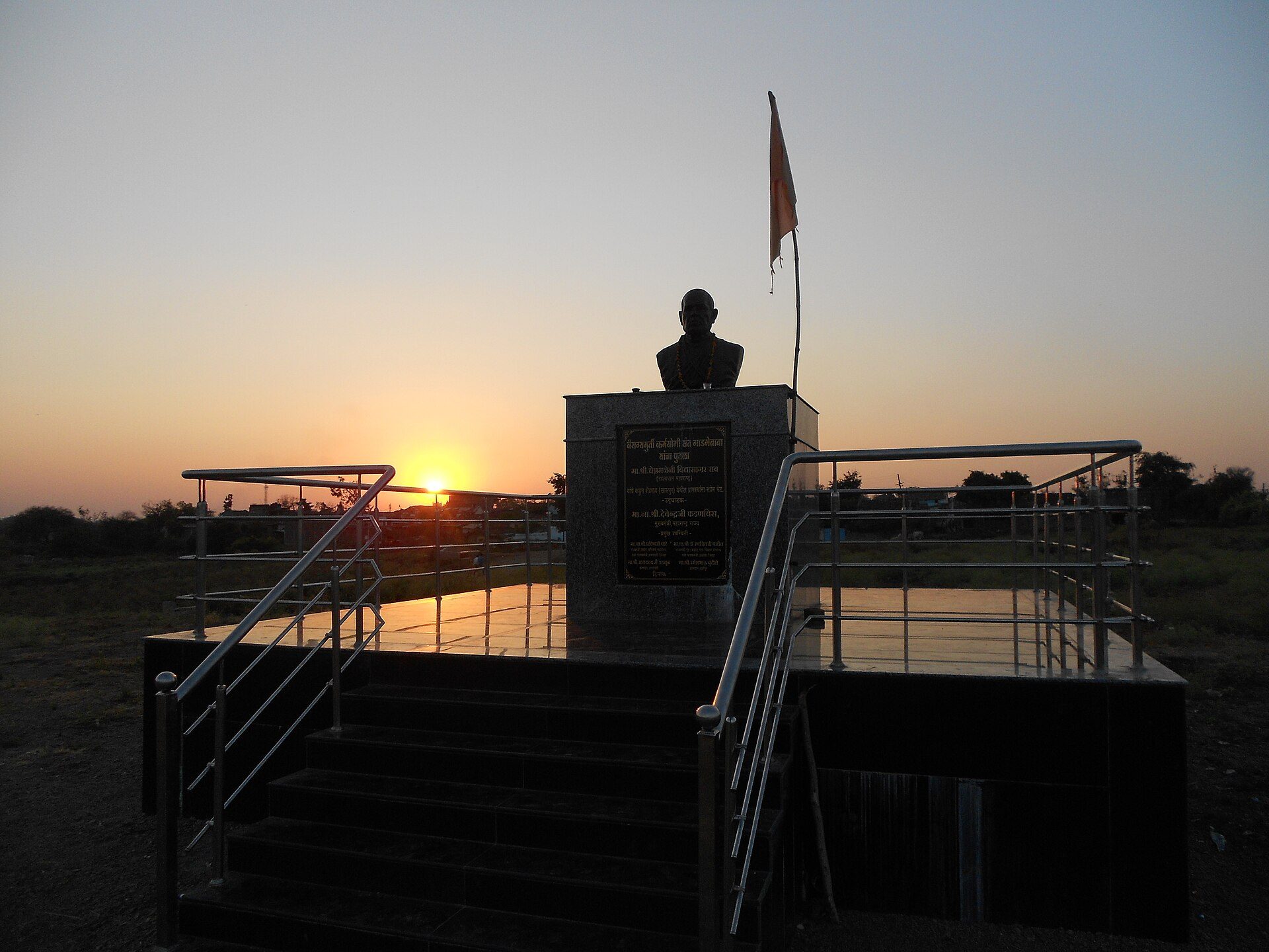 Silhouette of a bust on a stone pedestal against an orange sunset.