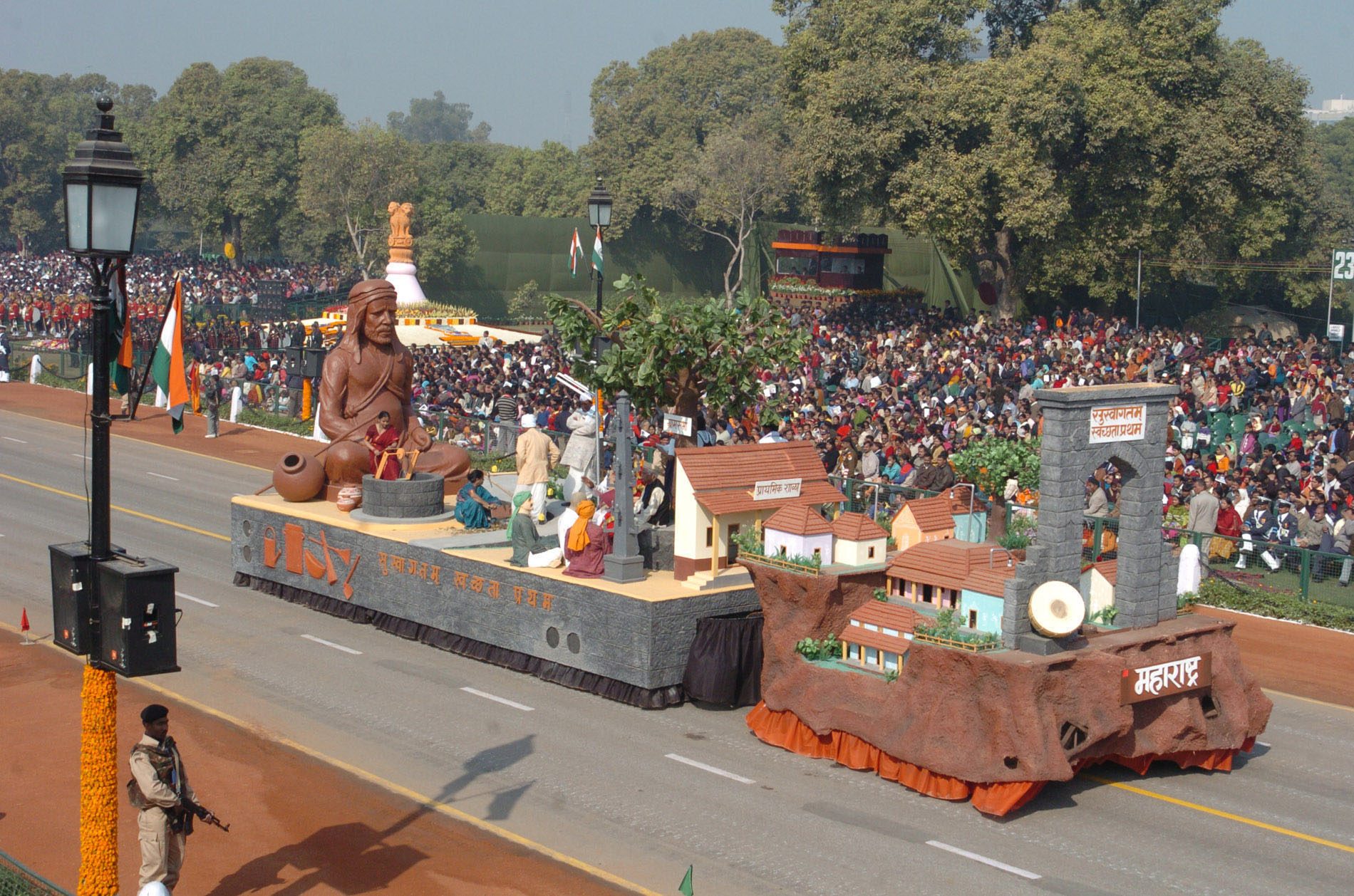 A parade float of Maharashtra showing a seated figure of Sant Gadge Baba, village houses, and a watching crowd.